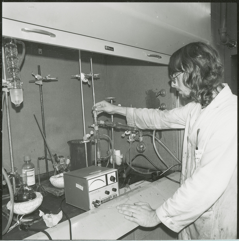 A researcher adjusts scientific equipment during an experiment. Several pieces of the equipment are attached to each other via tubes and other connectors. A control box is sitting in front of the glassware. This photograph was featured in the Chemical Engineering Brochure for 1978.