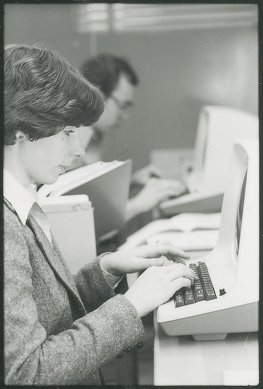 Two individuals enter data into early computers. background. This photograph was featured in the Chemical Engineering Brochure for 1980.