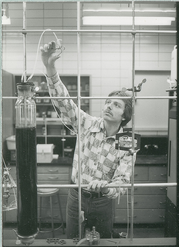 A young researcher with raised arm is adjusting a piece of equipment in a laboratory. This photograph is featured in a Chemical Engineering brochure, Jan. 23, 1980.