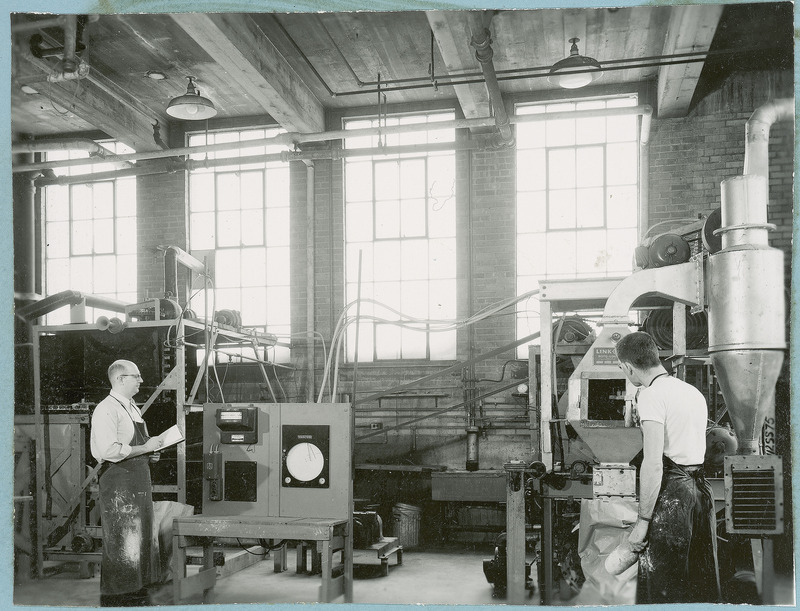 The researcher on the right is standing in front of the Link-Belt Roto Louvre Dryer used in sulphate fertilizer research in the West Chemical Engineering Building. The researcher on the left is standing in front of the control equipment taking notes.