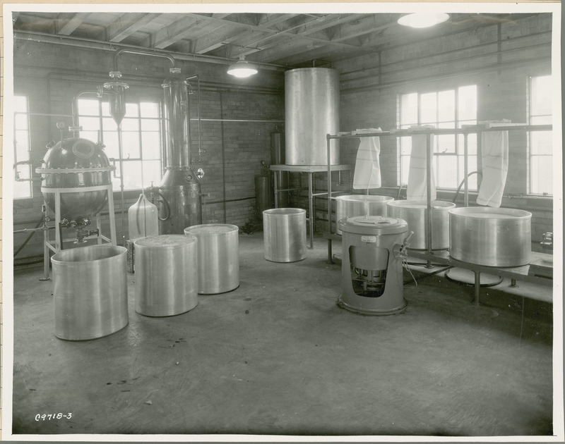 A group of large cylinders and tubes containing agricultural by-products are in the foreground. One of the cylinders is empty and waiting to be filled. There are towels hanging over the tubs and there is a large tank sitting on a table in the corner of the room.