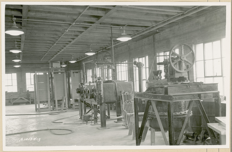 On the right side of the room are two large pieces of equipment. A group of coils are laying against one of the machines. Hoses are laying on the floor. Three wooden structures are in the background.