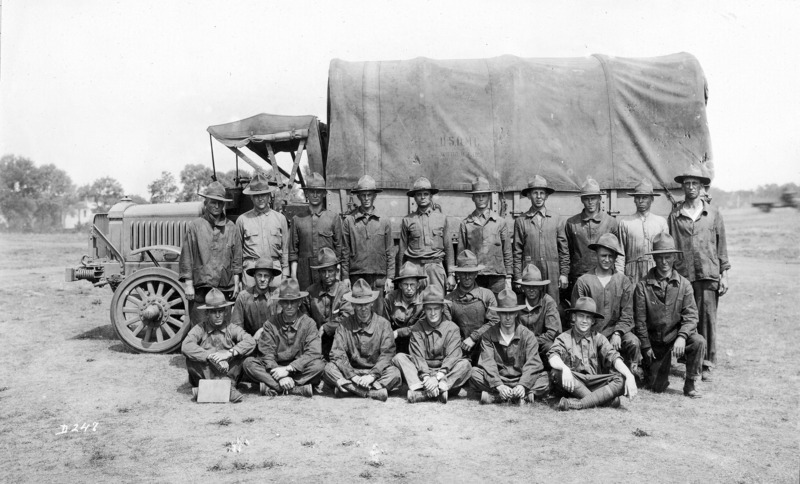 A unit of U.S. soldiers:"Second section, Iowa section." Twenty-three men are posed for a photograph by a military transport vehicle. The truck's canvas cover is stenciled with the insignia "U.S.Q.M.C.".