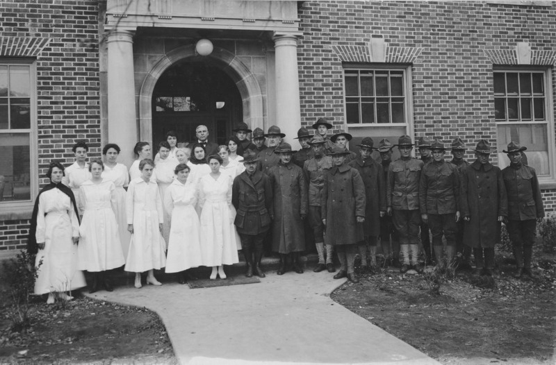 A military corps and hospital staff formal portrait in front of the Student Services Building. Eighteen uniformed men, fourteen uniformed female nurses, and one man in a suit are posed for the photograph.