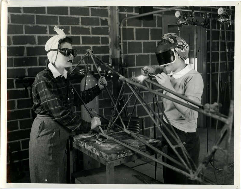 These cadettes with their hair wrapped in a turban and wearing eye protection, are working on the tail of a wrecked plane in the Welding Laboratory of the Mechanical Engineering Building. One of the projects for the five-week laboratory course was making a rudder pedal by welding the necessary parts.