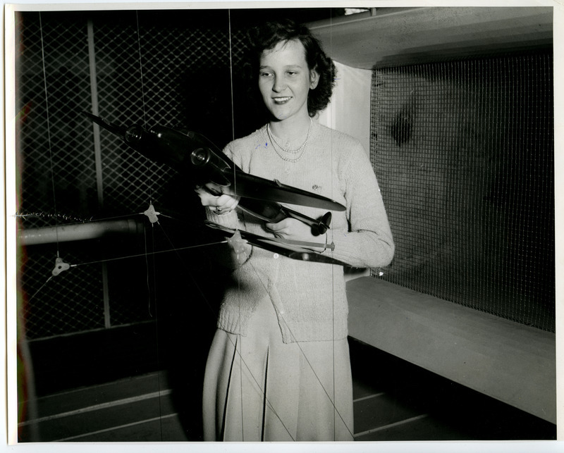 Betty Belle Gardner (Parsons, Kansas) is getting an advance taste of work in the wind tunnel in the Aeronautical Laboratory. She is about to replace a wing section in the mouth of the tunnel with a model transport plane.