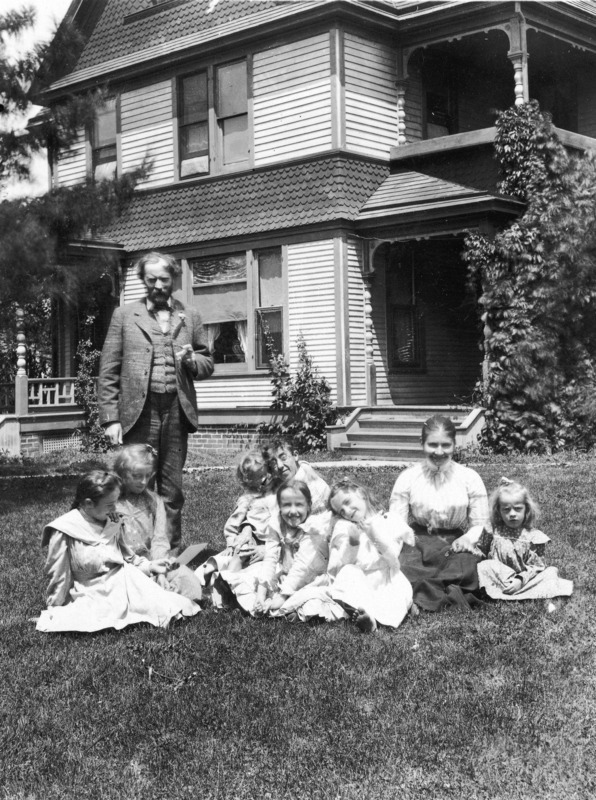 Dr. Pammel is standing outside his home in Ames, Iowa with his family seated on the ground in front of him.