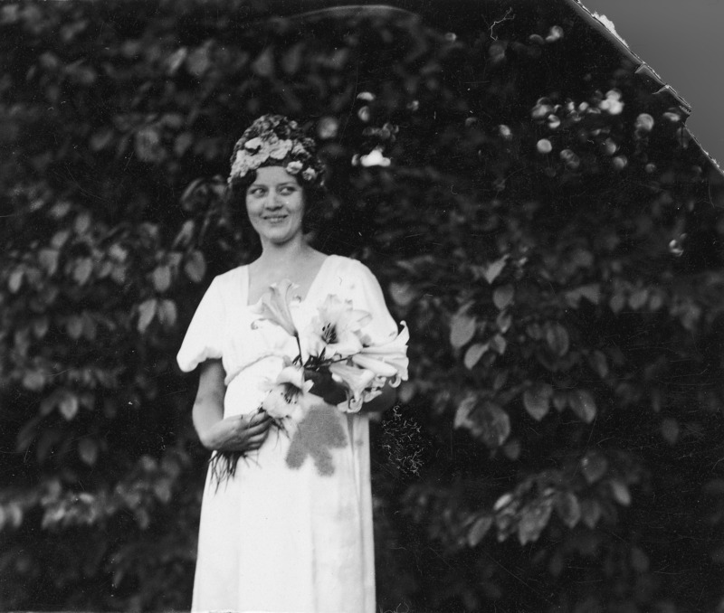 Josephine A. Bakke, director of Girls 4-H Club work in Iowa and wife of Dr. Arthur L. Bakke, plant physiologist and professor, is dressed for a special occasion. She is wearing a long dress and carrying a bouquet of lilies. There are flowers in her hair.