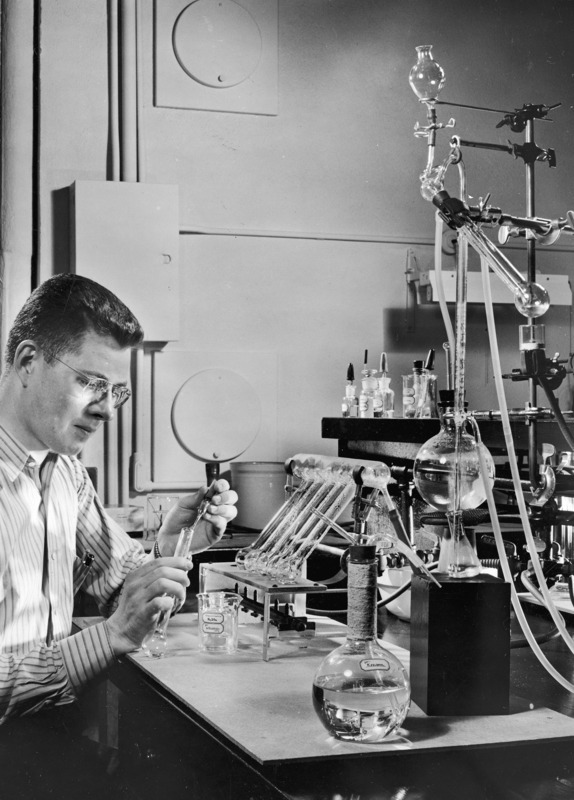 A student is working with a test tube conducting an experiment in the Micro-Chemistry Laboratory. A beaker and a flask have the name Kjeldahl written on them. H2SO4 is also written on the beaker.