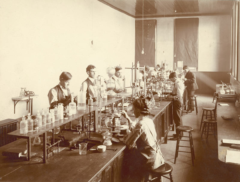 A quantitative analysis class in the Chemistry-Physics Hall, probably in the 1890s. The caption on the back of the photograph states: "Note blast lamp for igniting crucibles; Kipp gas generator; wash bottle made from round bottom flask.".