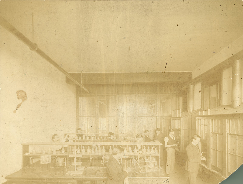 Nine men in the agricultural chemistry laboratory. The caption on the reverse reads:"Man on extreme right is T.W. Mast '97; next to him is Harry Scurr '98." The lower right corner of the photograph is missing.