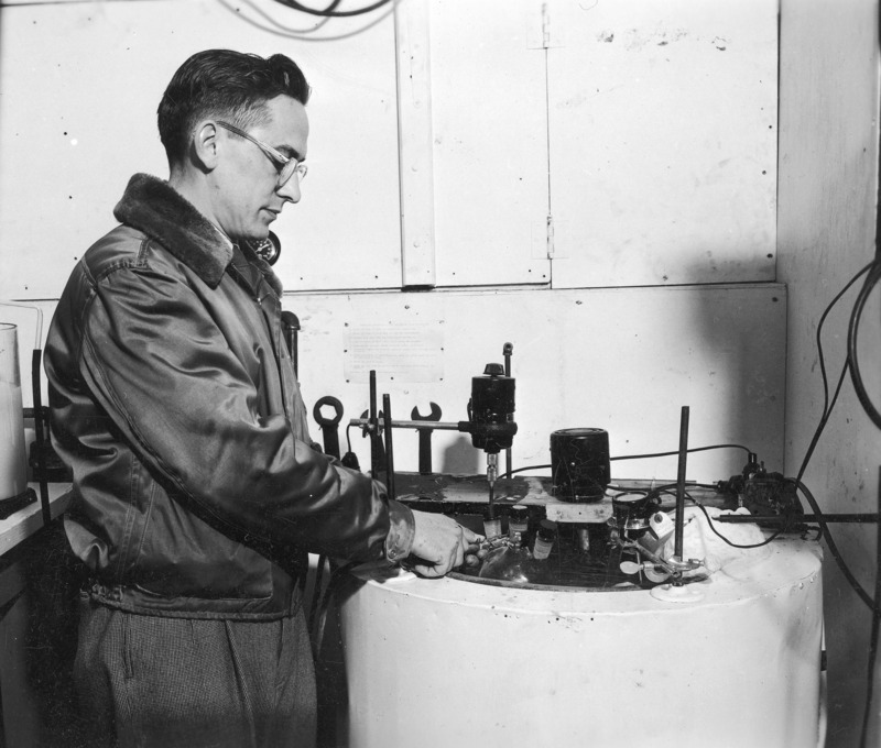 G. F. Hanna, a graduate student in the Department of Chemistry and a research fellow of the Agricultural Experiment Station, demonstrating the refrigerated bath in the refrigerated laboratory. The room was maintained at a temperature just above freezing and was used in preparation and fractionation of proteins, enzymes and other materials of biochemical importance that are frequently unstable at room temperature. The refrigerated bath provided even lower temperatures which might have been required for certain steps in processing. Research conducted in this facility was sponsored primarily by the Agricultural Experiment Station. It was located in the Biophysical Chemistry Laboratories in Chemistry Hall (now Gilman Hall).