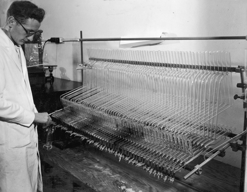 Frank Janssen, a graduate student in chemistry, with a Craig Liquid Extraction Apparatus. This apparatus, invented by Dr. Lyman Craig, an Iowa State alumnus, was widely used for separating medicinal and other biologically important materials. It performed in a single series of steps separations that would have taken many hundreds of steps if done using earlier methods. In this instance the apparatus was used to study Vitamin B12 and other important materials in biological chemistry.