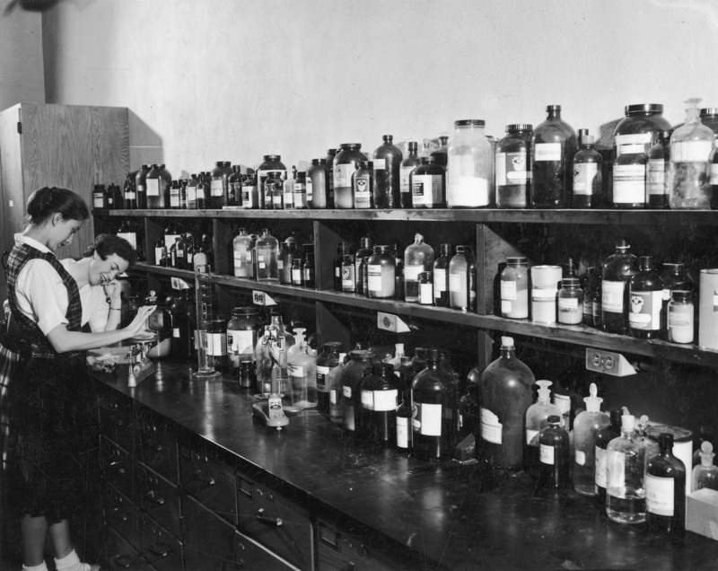 A chemical laboratory reagent supply depot. Two female students are posed at the far end of a counter as if selecting chemicals for use.