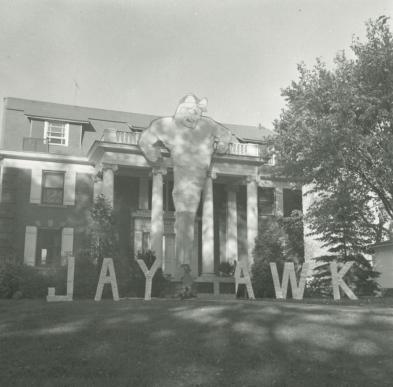 The Theta Delta Chi, Beta Deuteron Chapter, lawn display is located on the front lawn of their house. The central figure of the display depicts the head, arms and torso of a muscular male. The lower part of the figure tapers to a cyclone shape. On either side of this figure the word "Jayhawk" is spelled out in separate letters. The "h" is laying horizontal to the ground.