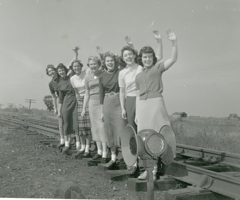 The 1950 homecoming court are standing in a single row beside a railroad track. They are: from left to right: Marlene Sidney, Janet Green, Pat Binder, Ethel Pearce, Betty Skyberg, Claire Schubert and Rita Dunn (queen).