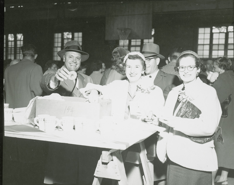 Three individuals are serving themselves donuts and beverages from a table at a Homecoming event. The table consists of a flat board resting on sawhorses.