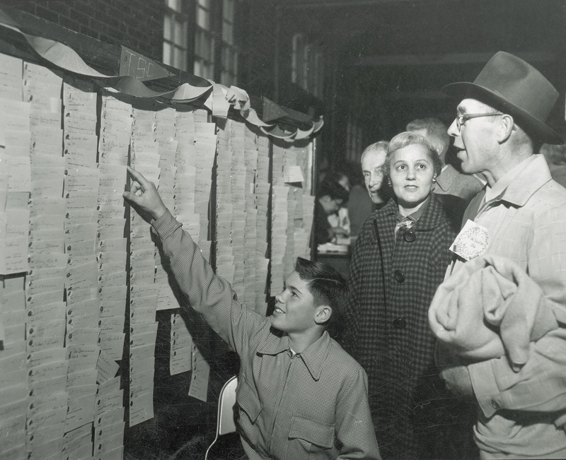 A group of three people are admiring a banner or possibly a registration board at the homecoming alumni luncheon.