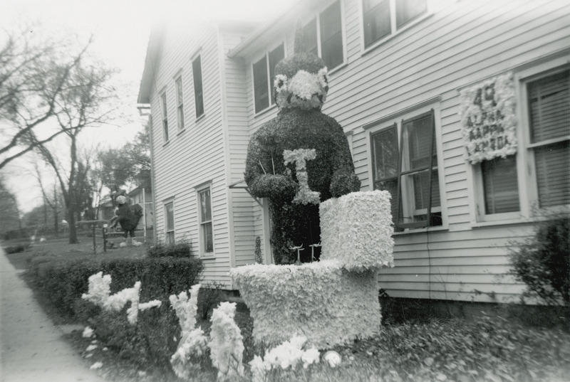 A large cardinal figure is using a toilet plunger to flush a Jayhawk down a toilet. Only the Jayhawk's legs and feet are protruding from the toilet bowl. A sign near the display read, "Alpha Kappa Lambda.".