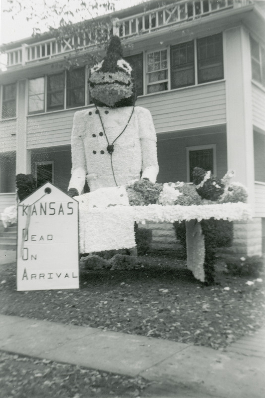 Cy the ISU mascot is dressed as a doctor and Jayhawk mascot lies on doctor's table with a football lodged in its head. There is also an attached toe tag reading "Kansas: Dead on Arrival".