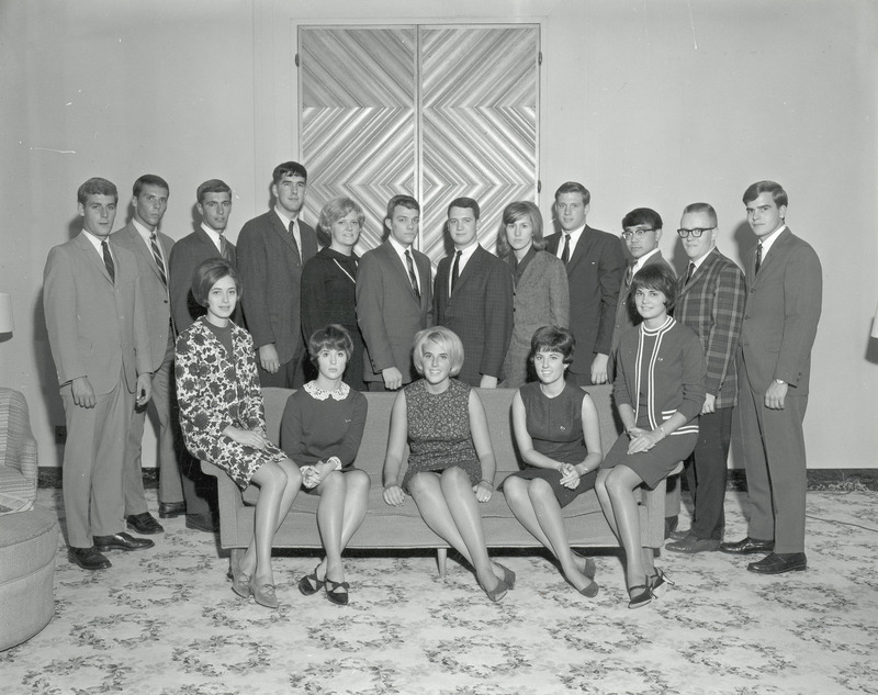 The 1966 Central Homecoming Committee is shown in a formal portrait. Five members are seated on a sofa while the other committee members stand in a row behind them.