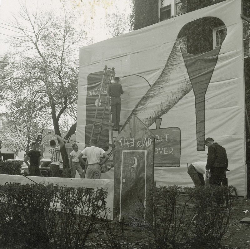 A large banner type lawn display is being constructed by several people. The central focus of the banner is a cyclone shaped cloud and a funnel.