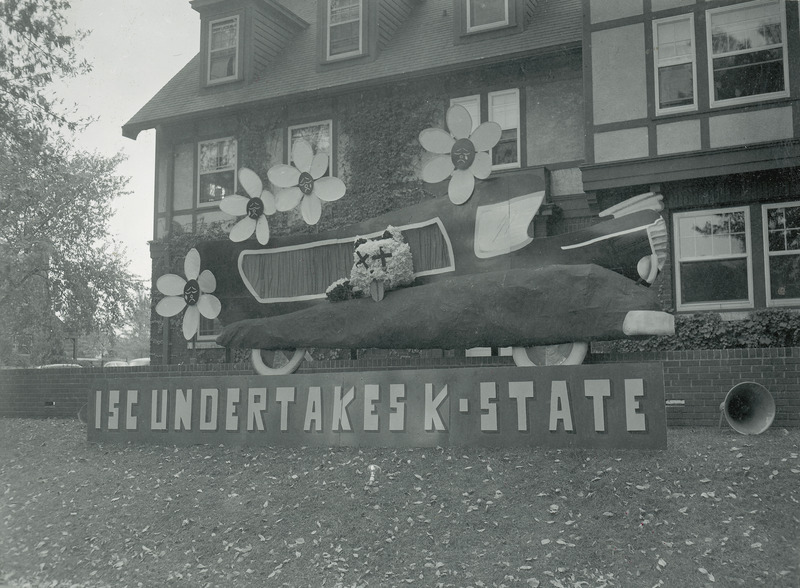 A comic hearse containing a wildcat figure is located behind a sign reading, " ISC undertakes K-State.".