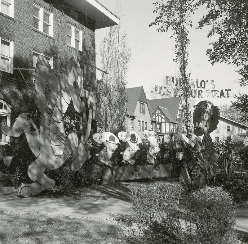 Two large cut out figures that resemble Pogo Possum and Albert the Alligator from the comic strip Pogo dominate this display along with three smaller pig figures. The alligator figure is carrying a knife and fork. The possum figure is sharpening a knife. A banner reading, "Buffalo's just our meat" hangs near the display. This display won first place in the Fraternity Division.