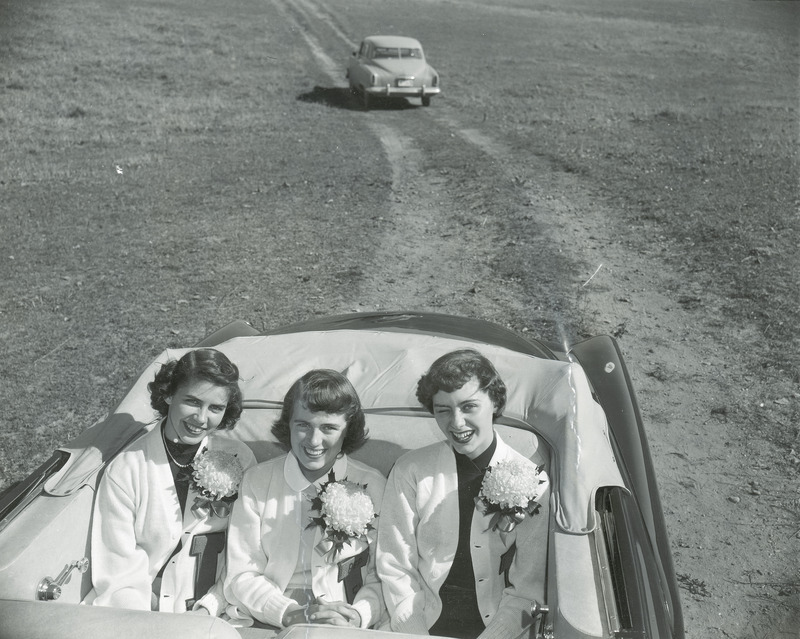 The Homecoming queen and her attendants are riding in the back seat of a convertible with the roof down. They are from left to right: Bonnie Helfrich, Doris Blair (queen) and Ann Bradley.