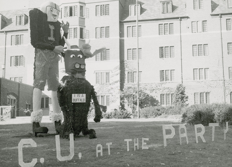 A large football player with the letter "I" on his jersey is standing behind a smaller figure of a buffalo. The buffalo has a sign around its neck saying, "I is a buffalo." Before the two figures the phrase, "C.U at the Party," is spelled out in separate letters.