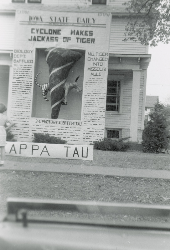 The Phi Kappa Tau, Alpha Omicron Chapter, homecoming lawn display is reminiscent of the front page of the Iowa State Daily student newspaper. The headline reads, "Cyclone makes jackass of tiger." The headline for a side column reads, "MU tiger changed into Missouri mule." In the middle of the "newspaper page" is a 3-D cyclone with the front part of a mule emerging from one side and the back end of a tiger on the other side.