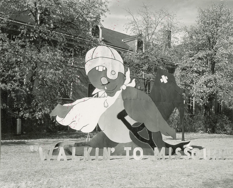 The central figure in this lawn display is a cardinal type bird with one wing in a sling and a crutch under the opposite wing. It wears an old leather football helmet and appears to be crying.