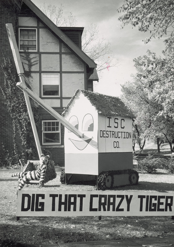 A three-dimensional steam shovel resembling the illustration from a children's book is scooping up a tiger in its bucket. The steam shovel has a smiling face painted on one end and one side is labeled, " ISC Destruction Co.".