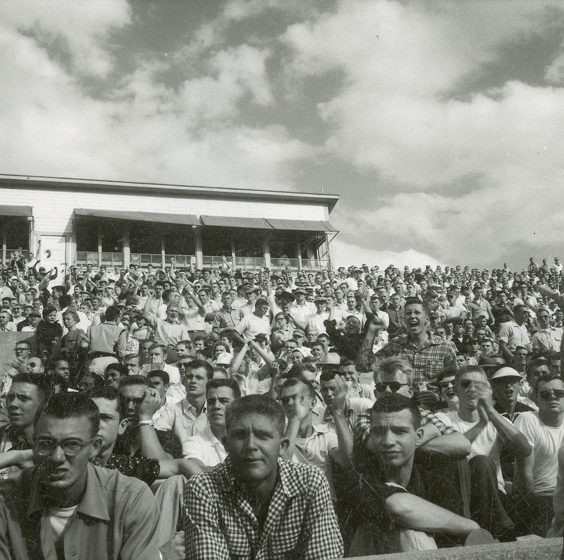 A group of students are seated in bleachers watching a Homecoming activity, quite possibly the football game.