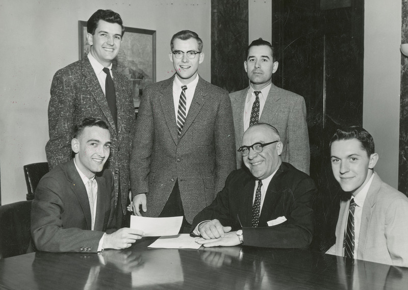 James A. Hilton is seated at a table surrounded by five young men. They are: Front row (left to right): Unidentified committee member, James A. Holtin, unidentified committee member; Back row (left to right): Larry E. Barnes, Jan Rakow, Dr. Darrrel Metcafe. The Committee is presenting Dr. Hilton with a check for $1500.00 for Hilton's Dream Center which later became the Iowa State Center.