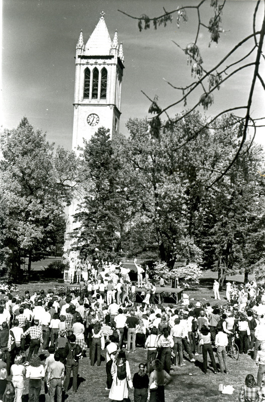 Students are on a stage performing in front of a crowd in the "Yell like hell" competition. The Campanile is in the background.