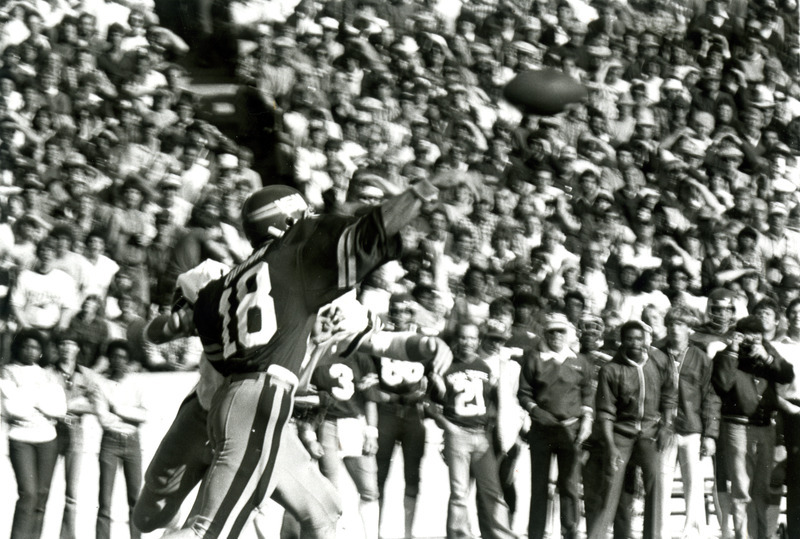 Quarterback, John Quinn, wearing jersey no. 18 throws the football as the crowd looks on.