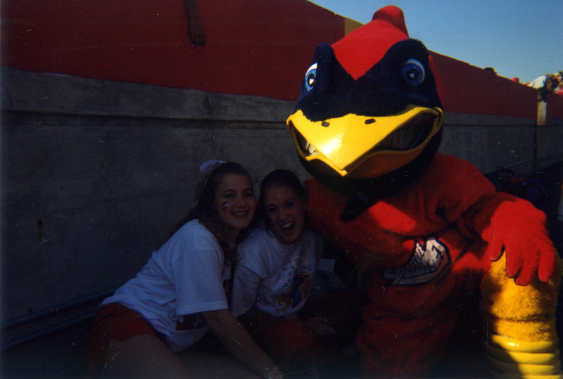 Two cheerleaders are posing for a photo with CY.