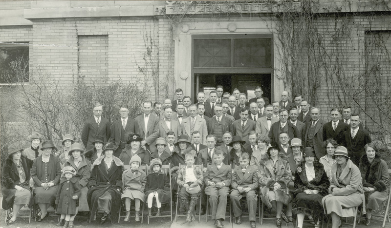 A group of Alumni and their families gather for a group photo in front of the Dairy Building.