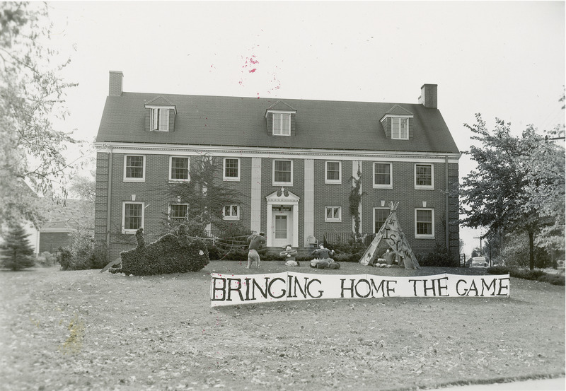 Alpha Gamma Delta, Rho Chapter's lawn display, first place winner in the sorority division, shows a buffalo being dragged by an Iowa State football player. Another player is seated at the opening of a tepee and two other players are sitting on the lawn. A banner reading, "Bringing home the game", is at the front of the display.