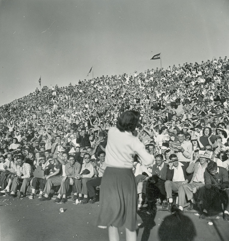 A cheerleader is leading the crowd in a cheer at a Homecoming activity.