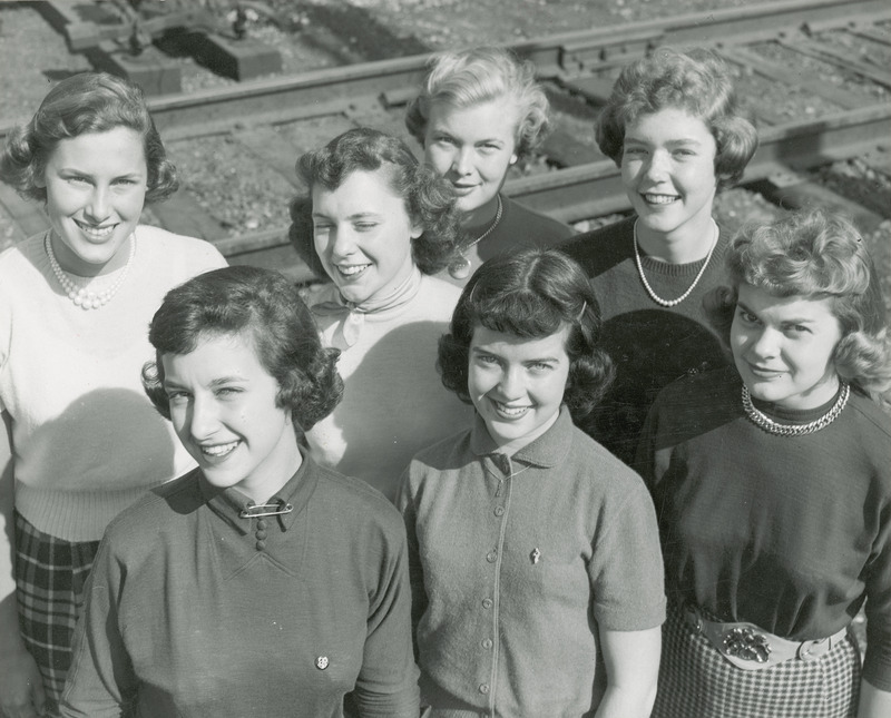 The 1950 homecoming queen candidates are posing in front of a railroad track. They are front row (left to right): Janet Green, Sac City; Rita Dunn (Queen), Sioux City; Betty Skyberg (Attendant), Canton, SD; Back row (left to right): Pat Binder, Barrington, IL; Claire Schubert, Maywood, IL; Ethel Pearce (Attendant), Mesa, AZ; Marlene Sidney, Davenport.