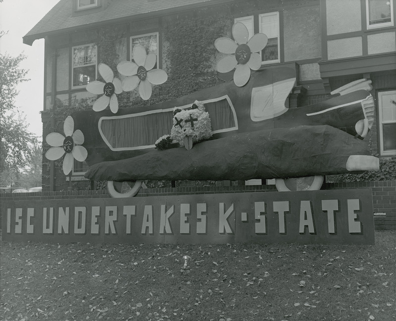 A comic hearse containing a wildcat figure is located behind a sign reading, " ISC undertakes K-State" in this Kappa Delta, Sigma Sigma Chapter lawn display.