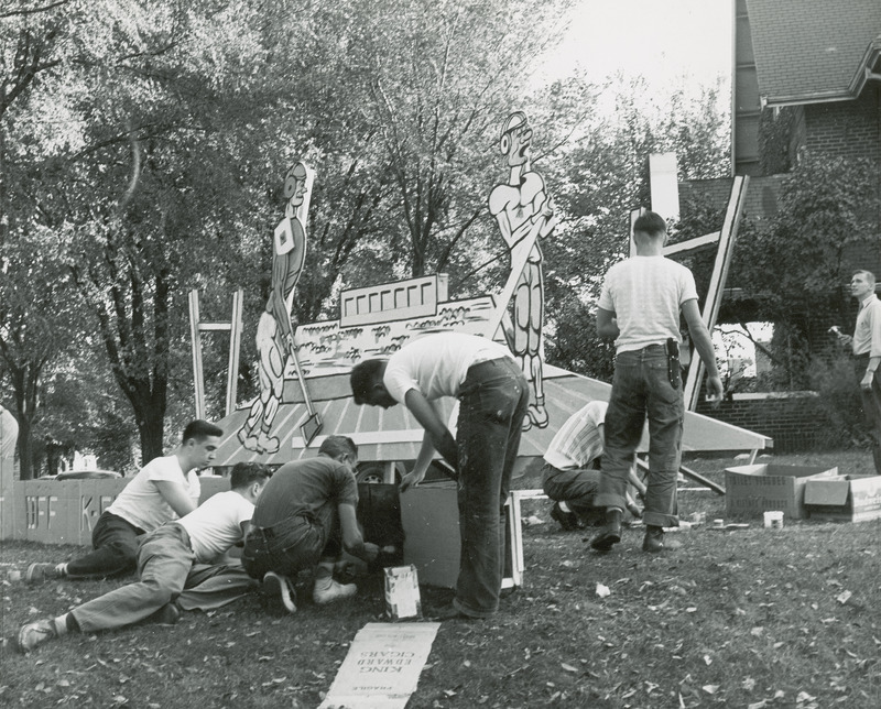 Several male students are working on a lawn display at the Delta Chi house.