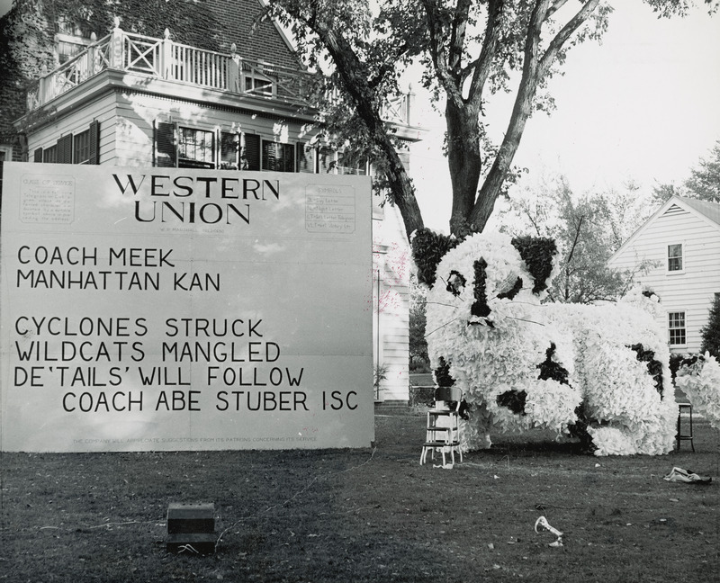 A large cat figure is the central focus of the Delta Delta Delta, Omega Delta Chapter's lawn display. Next to the cat is a sign which is formatted like a telegram reading, "Western Union, Manhattan, Kan., Cyclones struck, wildcats mangled, De 'tails' will follow, Coach Abe Stuben, ISC.".