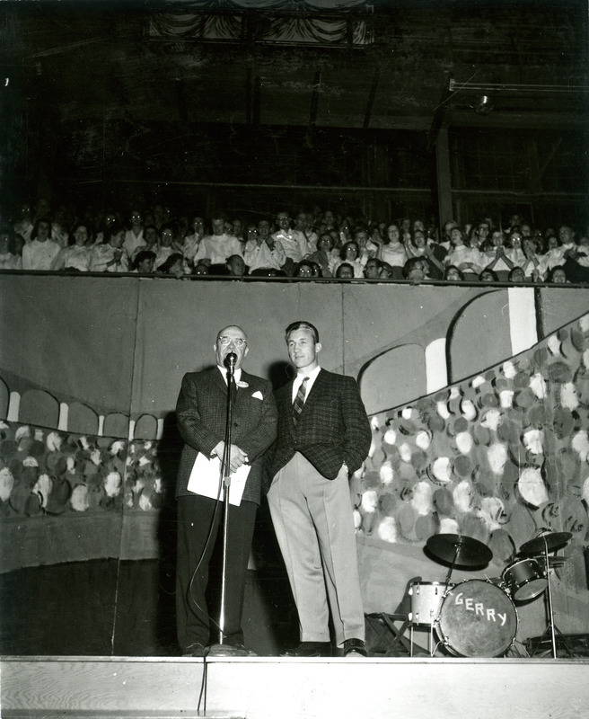 President Hilton is speaking to the crowd at the Homecoming Barbecue at the Armory as Coach Jim Meyers looks on.