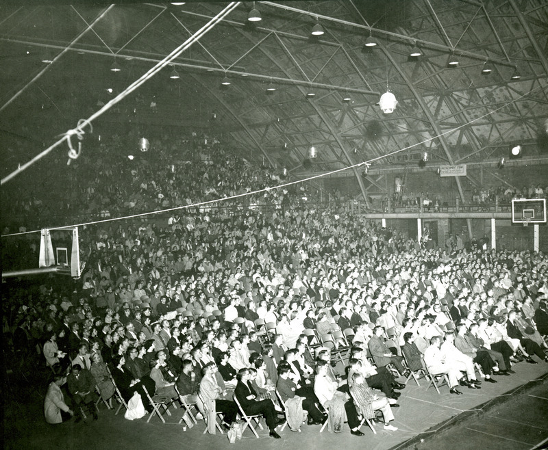 The crowd is seated listening to a speaker at the Homecoming Barbecue in the Armory.