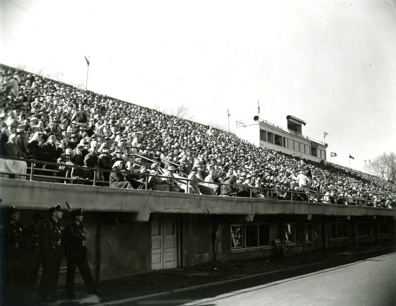 The fans are sitting in the bleachers while security officers look on from below the stands.