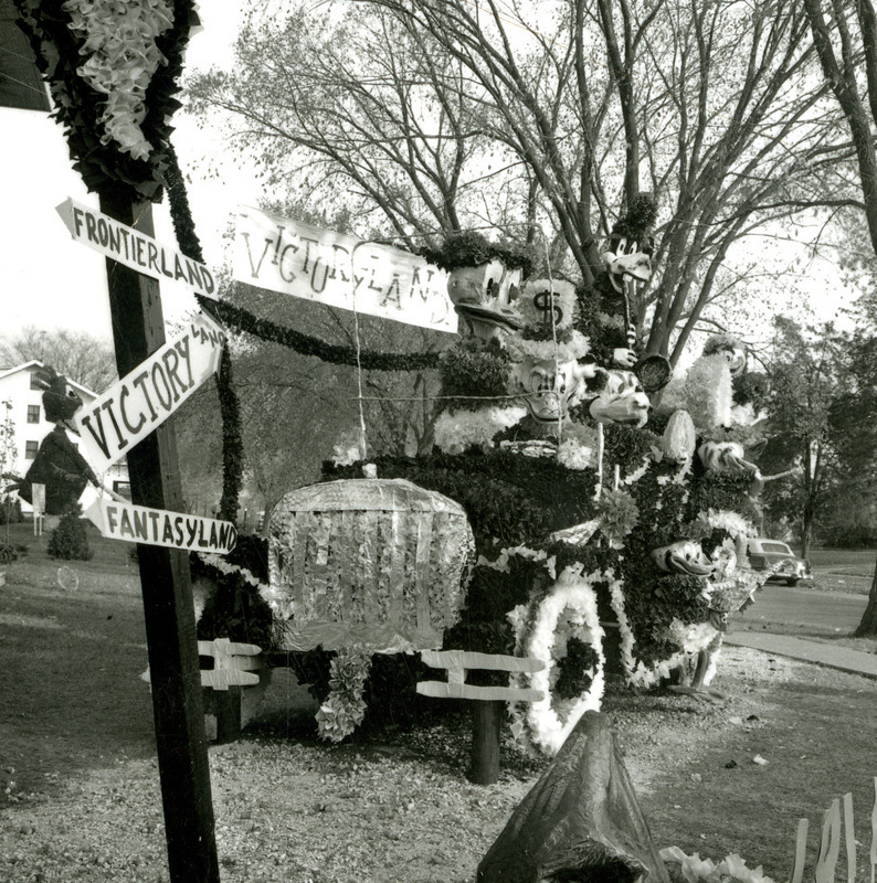 In the Phi Delta Theta homecoming lawn display, Disney characters including Scrooge McDuck and Mickey Mouse ride with Cy in a jalopy heading for a signpost pointing to Victoryland, October 1961.