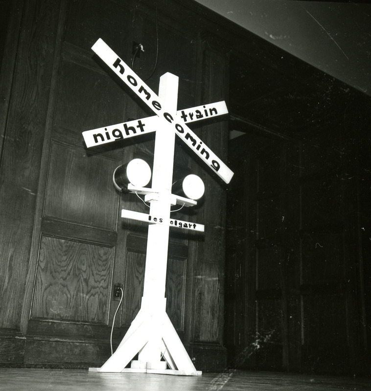 Homecoming Dance railroad crossing decoration has arms labeled Homecoming, the dance theme of Night Train, and the name of the band, Les Elgart, known for its song Night Train, 1965.